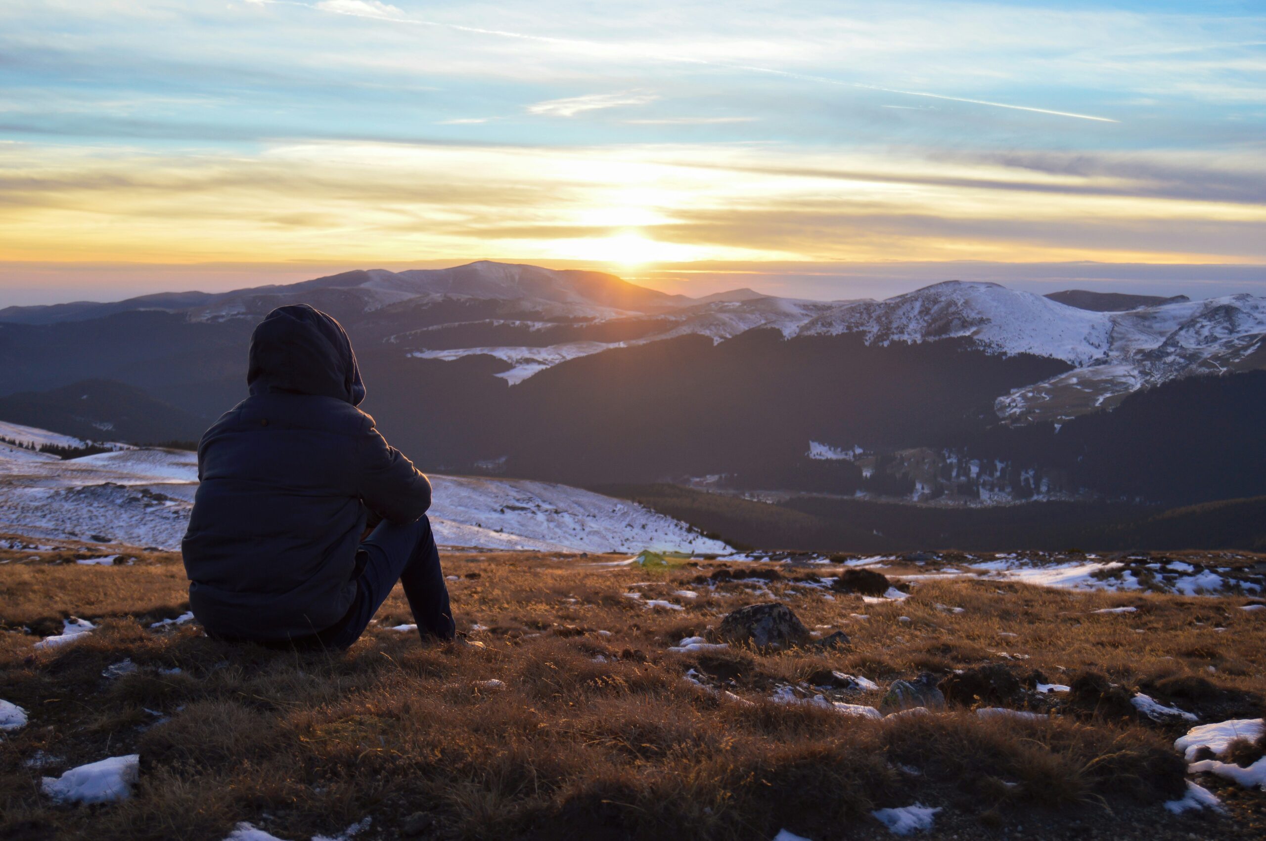 Person sitting on a grassy area, overlooking mountain with some snow, feeling regulated and calm