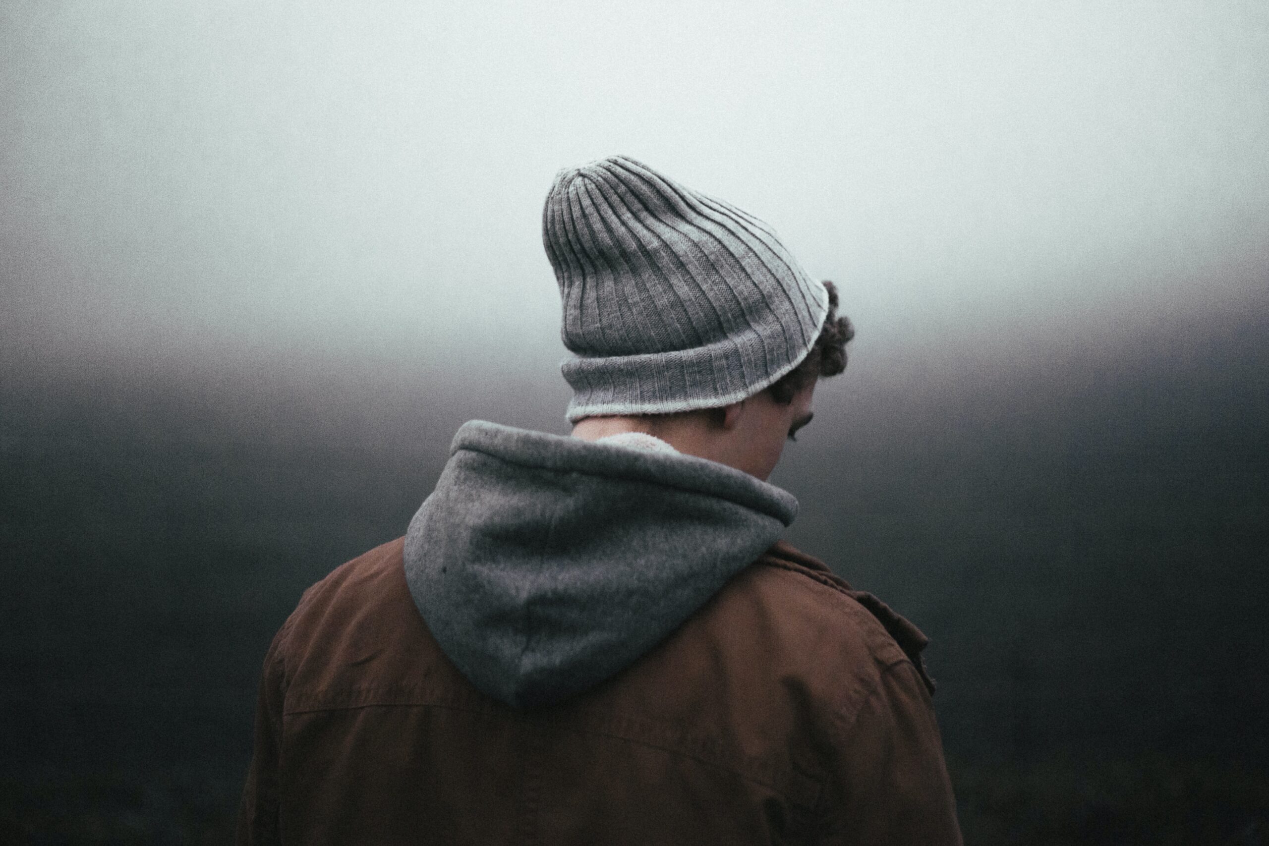 Male presenting person with a stalking cap on outside in the cold, image from behind. Depressed. Seasonal Affective Disorder. Seasonal Depression
