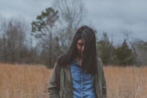 A female presenting Indian woman with her head down, outside, experiencing depression.