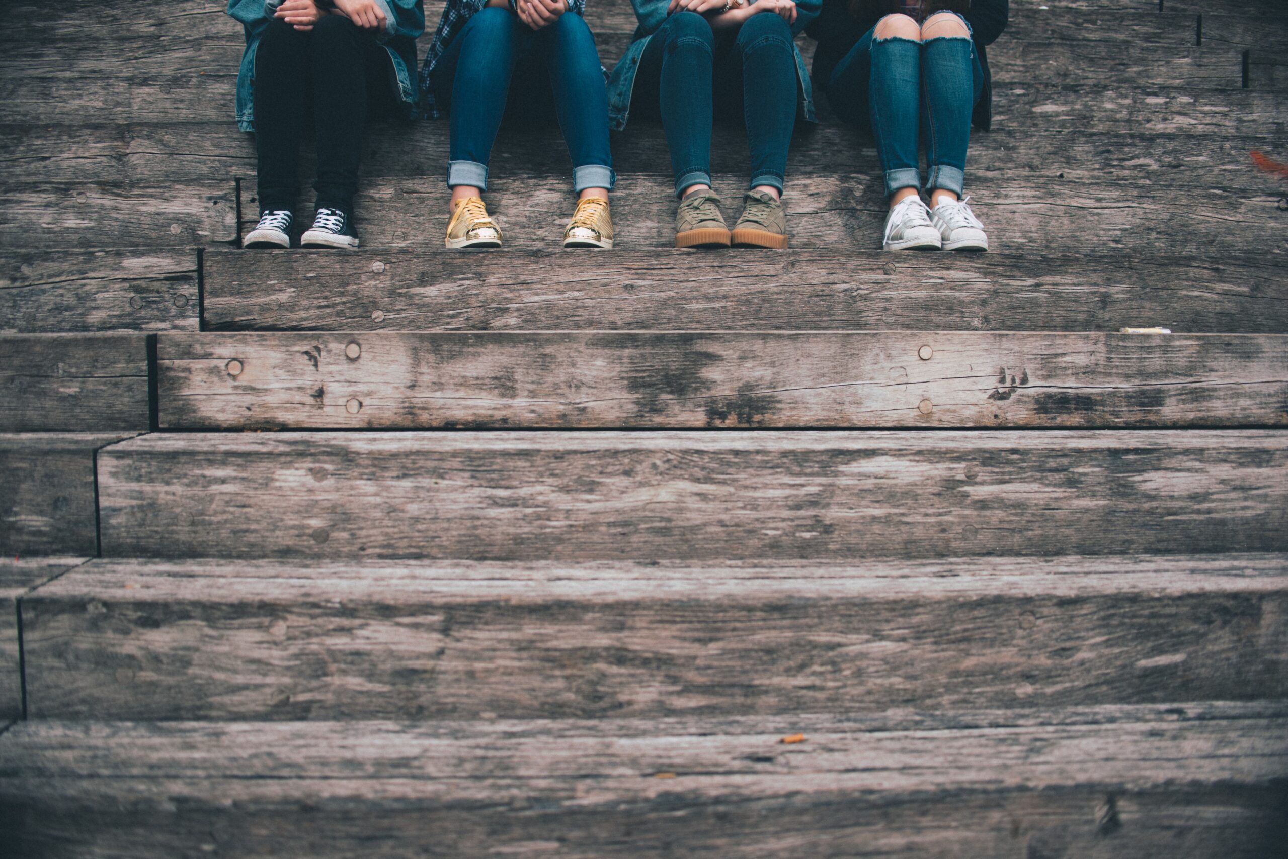image of four pairs of teen legs in jeans and shoes on the top of a set of stairs outside.