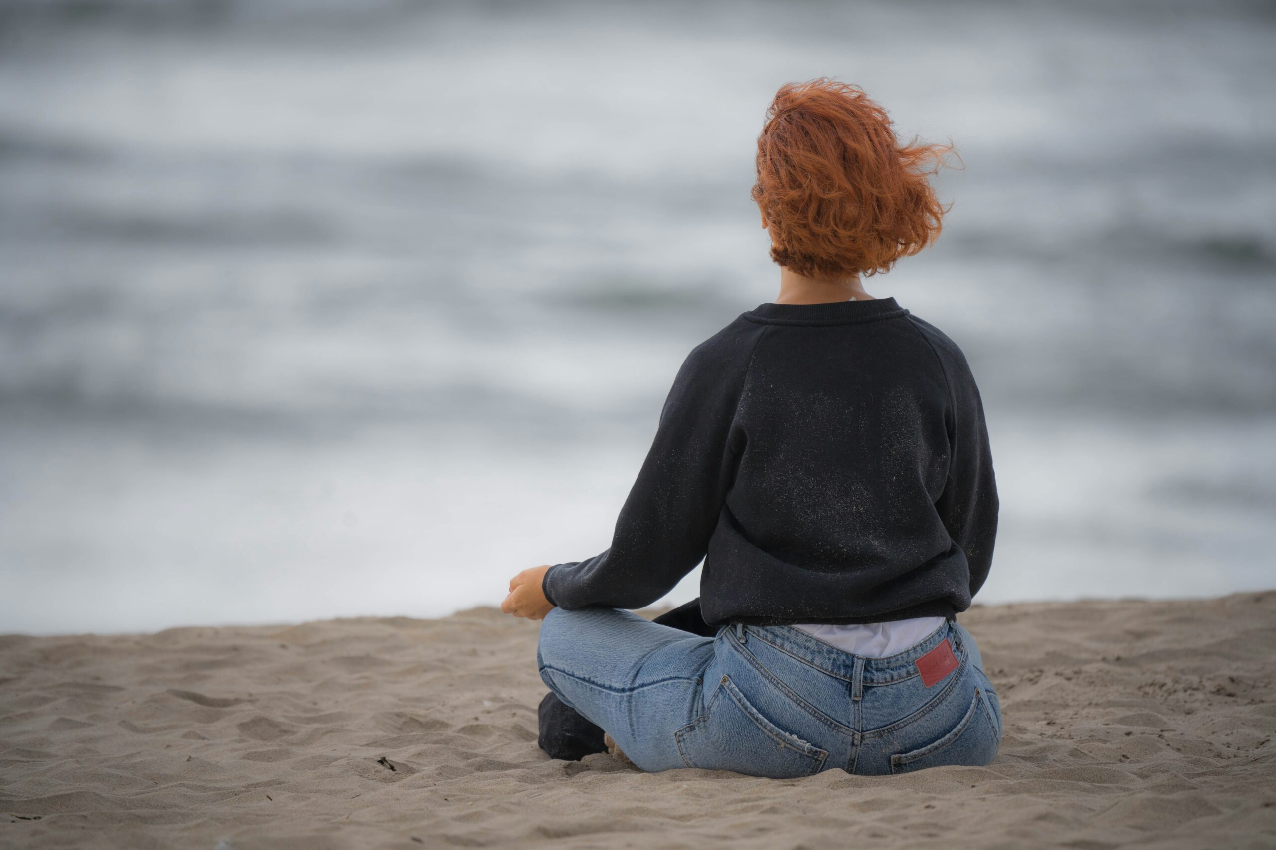 Person sitting on a beach, taking deep breaths, being present with mind-body connection, practicing polyvagal exercises