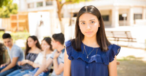 Image of a teen girl looking at the camera with friends busy behind her. 