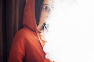 girl exhales a lot of vapor, a white cloud with light space. Substance abuse therapy for teens 