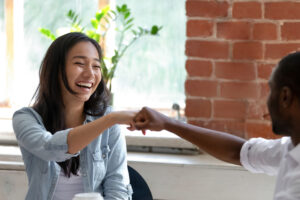 Image of Asian female smiling and Black male colleagues fist bumping.