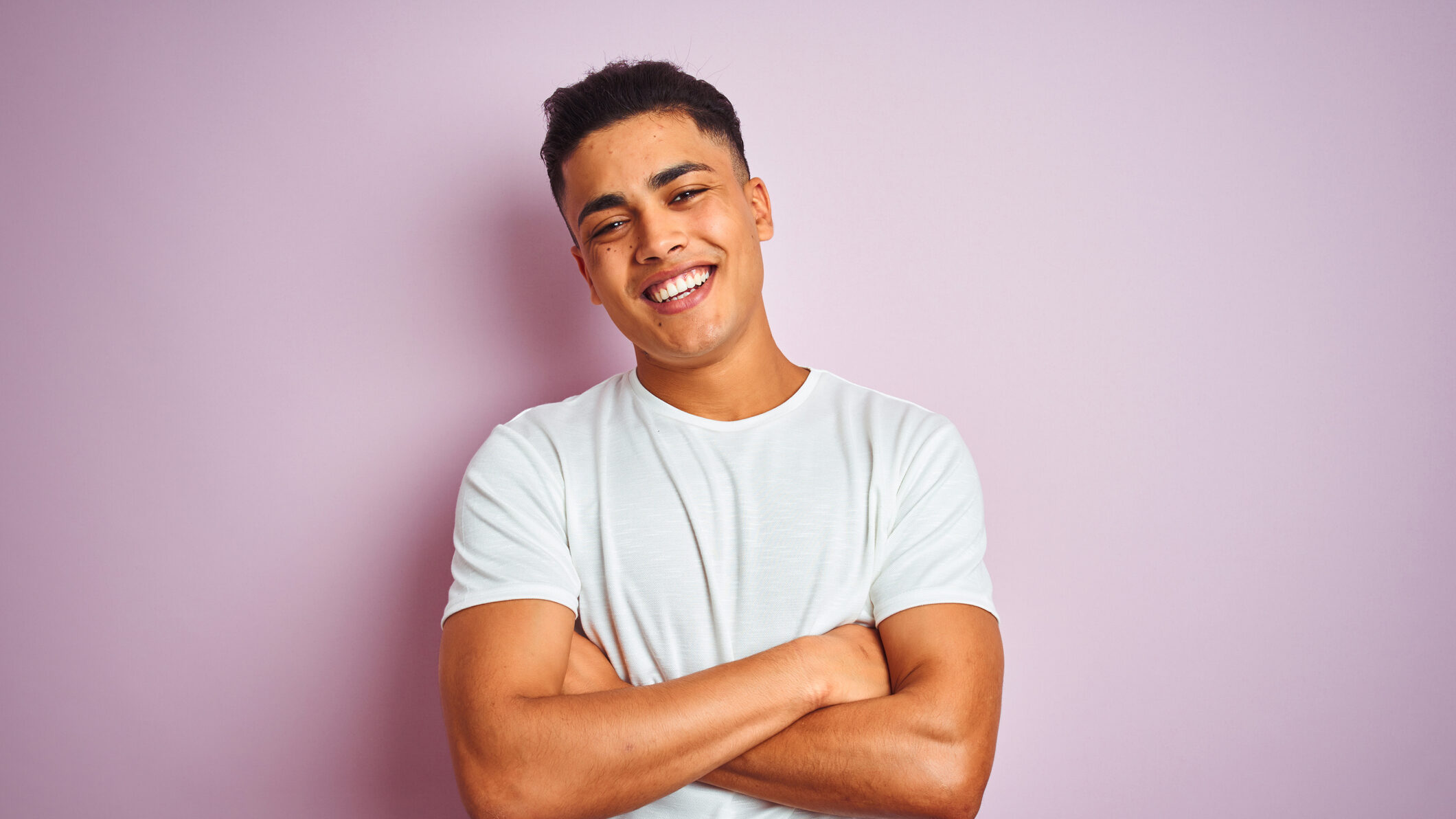 Asian man smiling at camera in a white t-shirt, arms crossed, pink background"