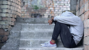 Image of a lonely male teen sitting building stairs with hood up and head buried in lap. 