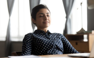 Relaxed young Latina business woman relaxed, sitting at work with laptop at desk with eyes closed