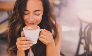 Image of a woman enjoying cappuccino in a street cafe.