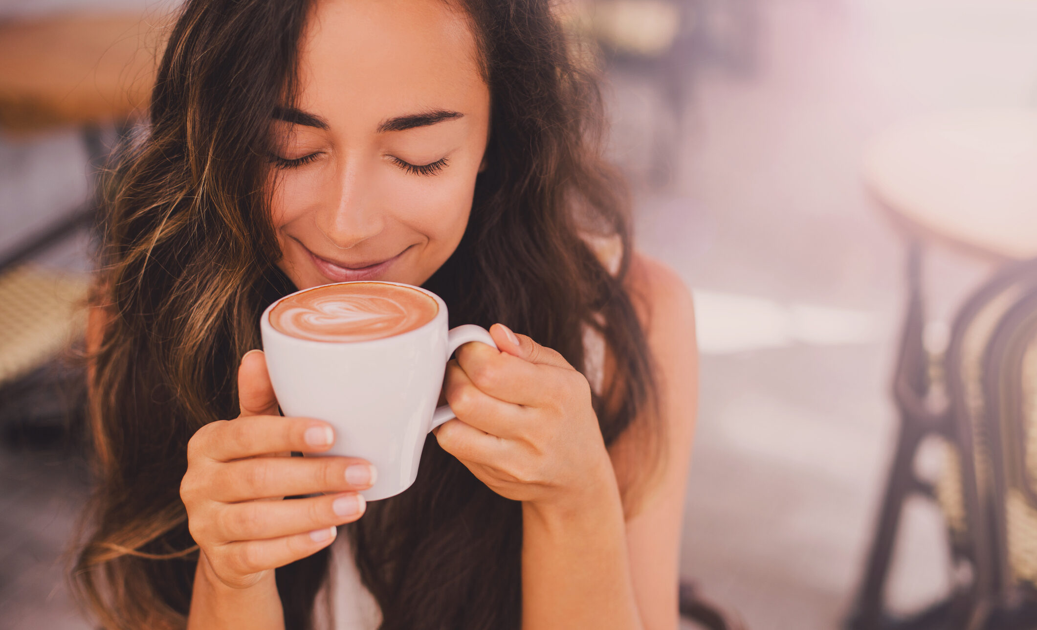 Young beautiful happy woman with long curly hair enjoying cappuccino in a street cafe