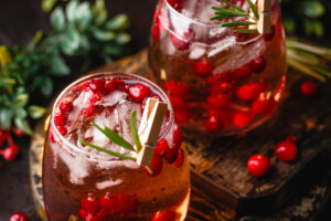 Festive cranberry and rosemary mocktail with ice on the dark background.