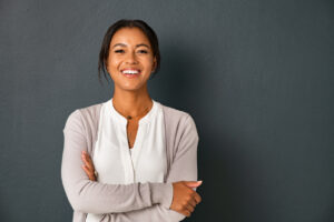 Beautiful mid adult african american woman standing on grey wall with crossed arms. Mature indian woman isolated on gray background. Portrait of smiling hispanic lady looking at camera with satisfaction.