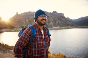 A young adult backpacker smiles as the move through resistance at the lake view with sunset behind him in the mountains