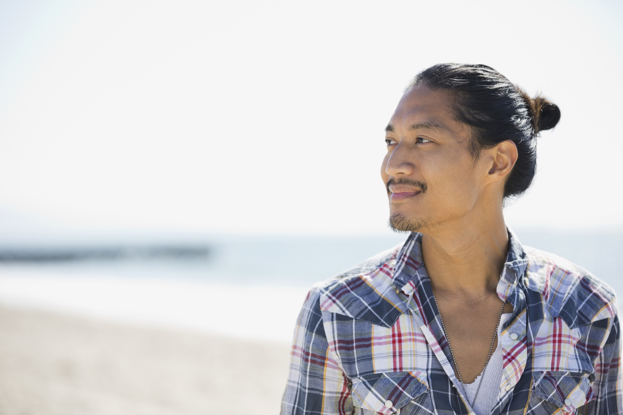 Thoughtful Asian man with man bun looking away on beach. Man finding hope