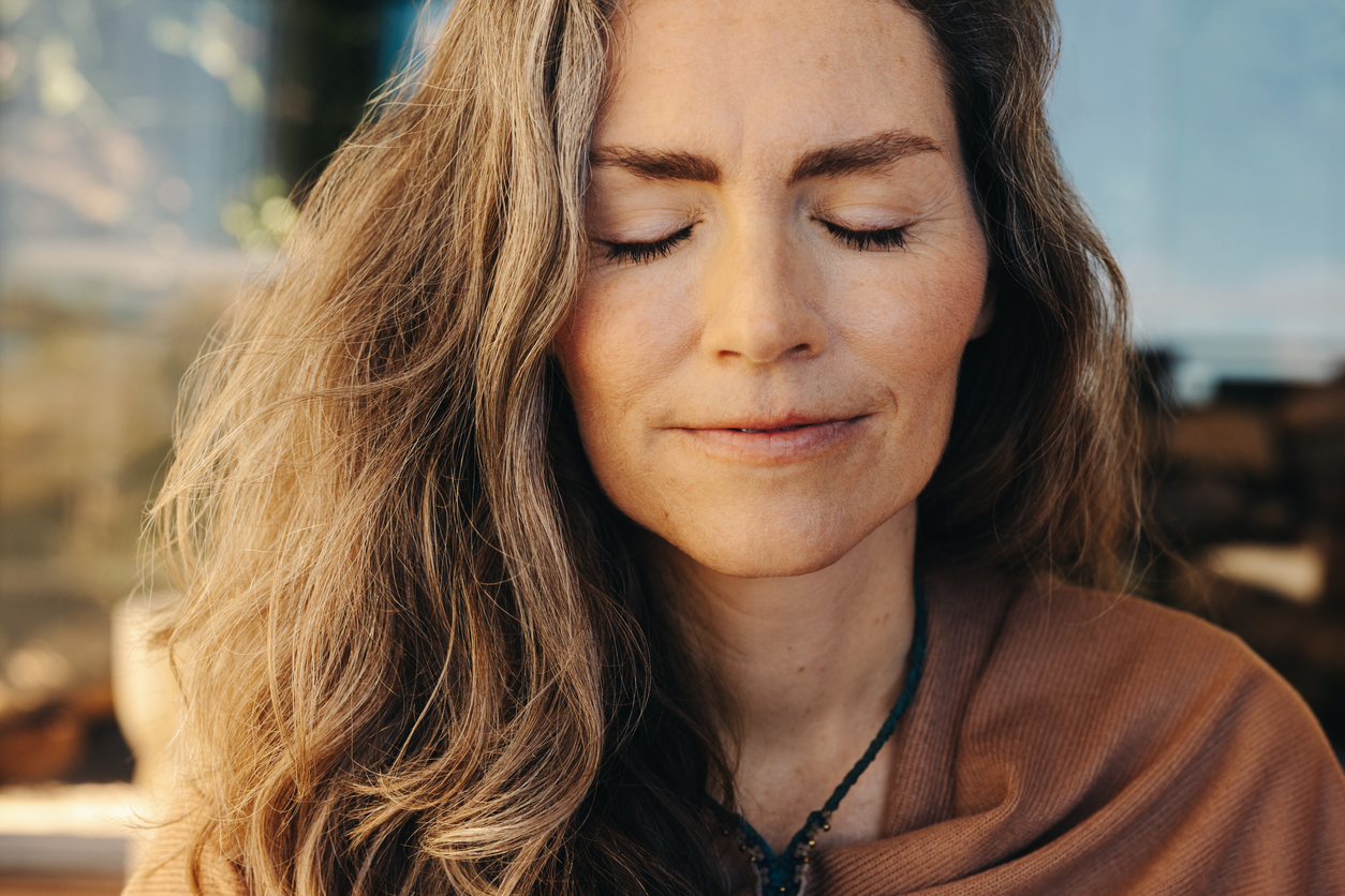 Woman outside in nature, sitting mindfully with eyes closed, feeling gratitude for trauma therapy