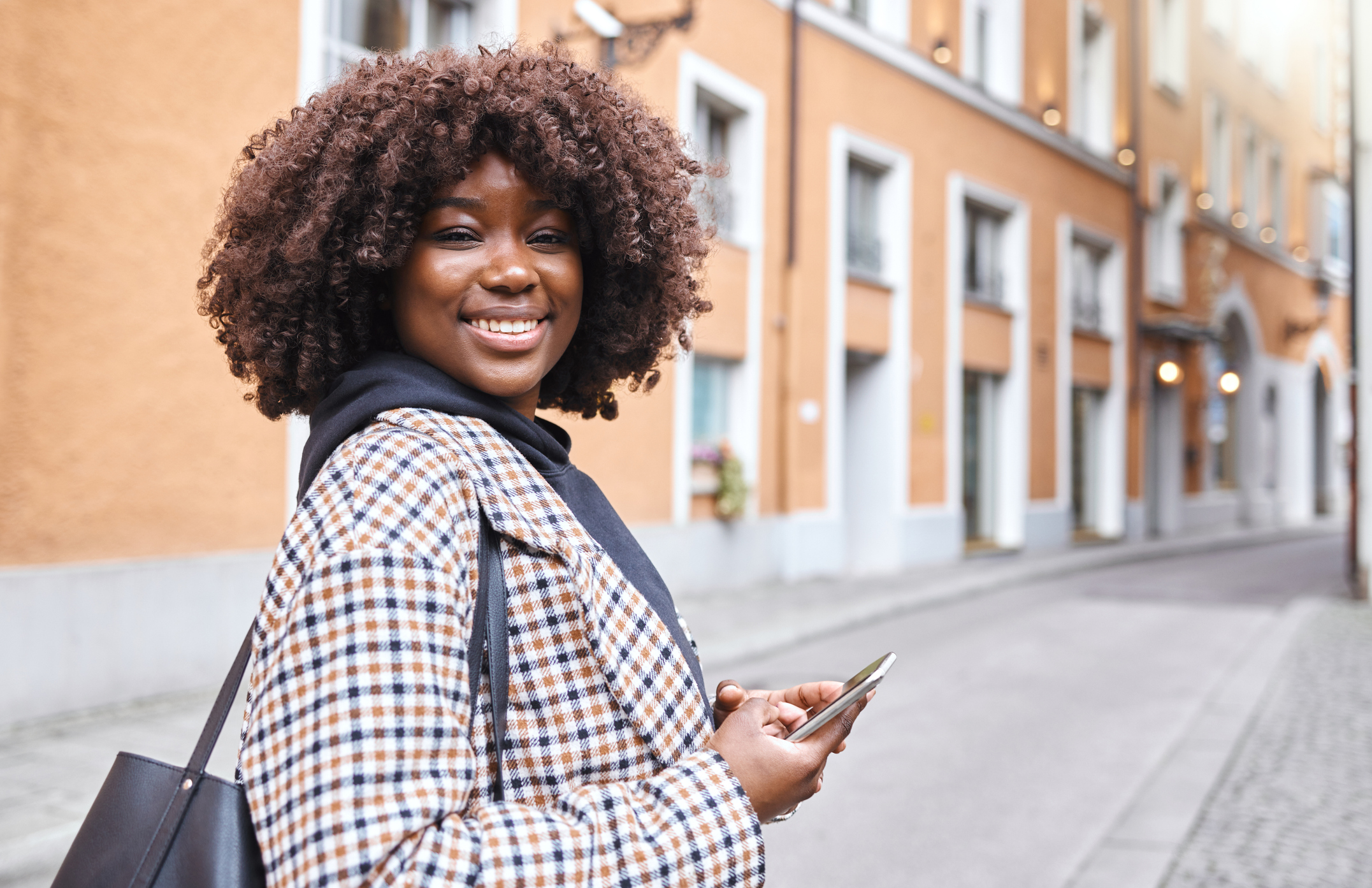 Portrait, phone and mockup with a black woman in the city for travel, tourism or adventure overseas. Smile, mobile and mock up with a female traveler outside in a foreign town on an urban background