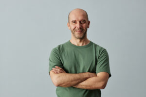 Man smiling with arms crossed in green t-shirt after therapy talking about relationships. 