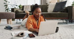 Black female looking for therapist on laptop. Lying on carpet infant of couch. relaxed and smiling