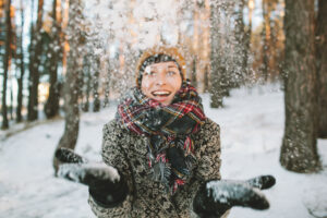 Young woman in winter forest having fun with snow falling in hands