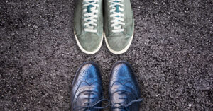 Image of a pair of sneakers and a pair of dress shoes facing off on pavement. View from above.
