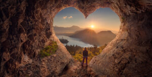 Image of a lone woman enjoying looking tour a large, heart-shaped rock formation at the sunset over mountains.