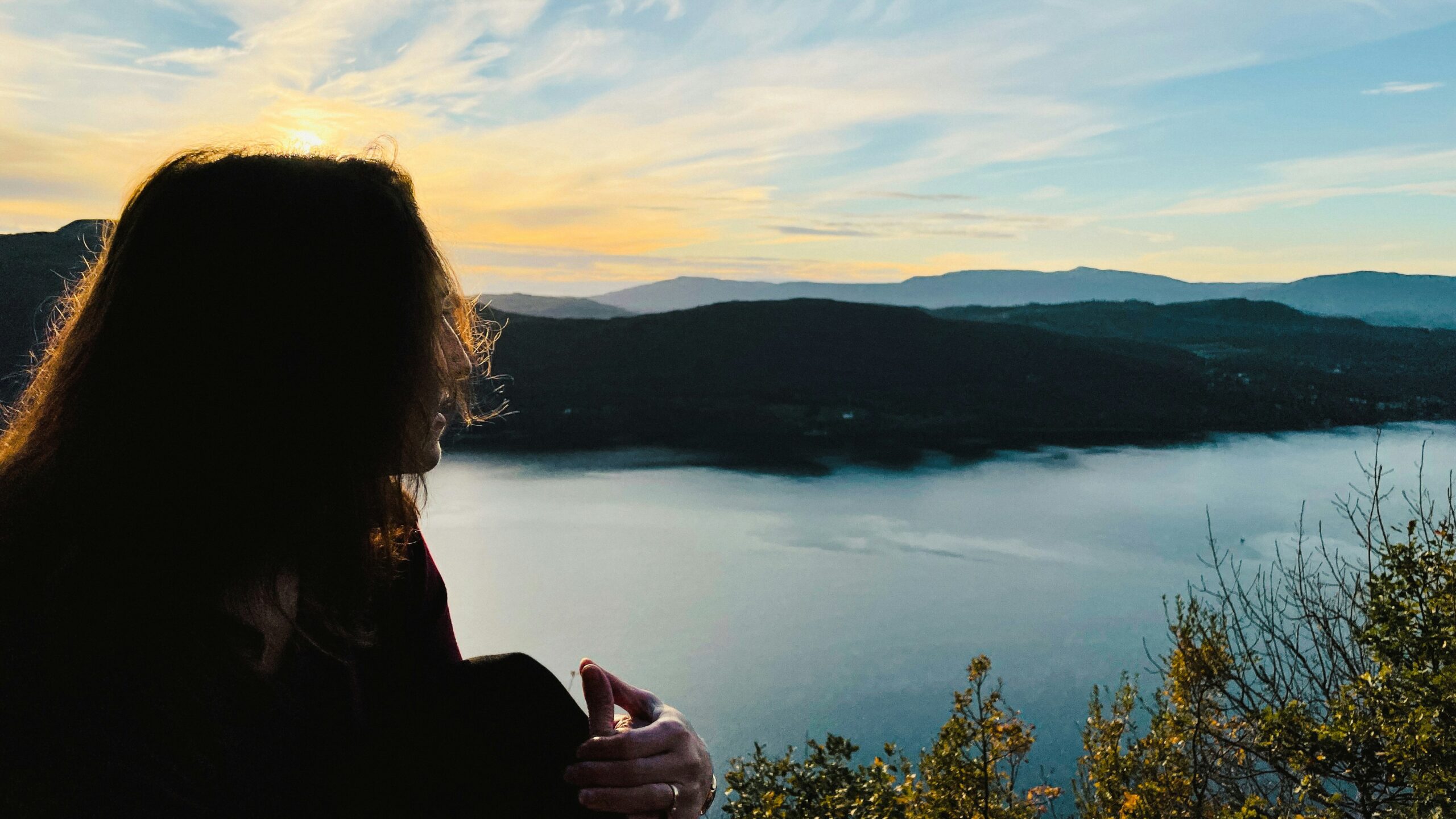 Profile of a woman sitting on the banks of a lake in the mountains pondering dating