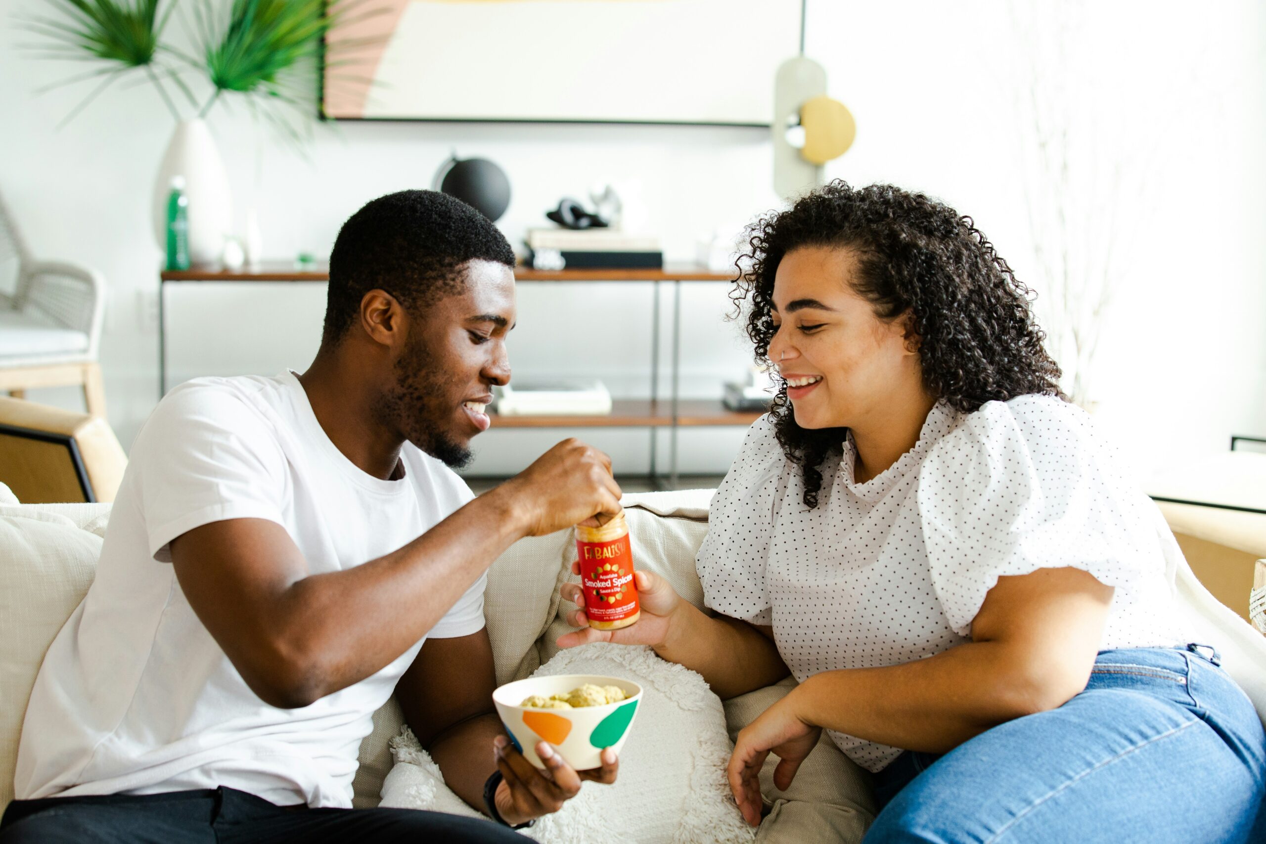 A Black male and Black female sitting on a couch sharing a snack. Dating. Dating with Anxiety