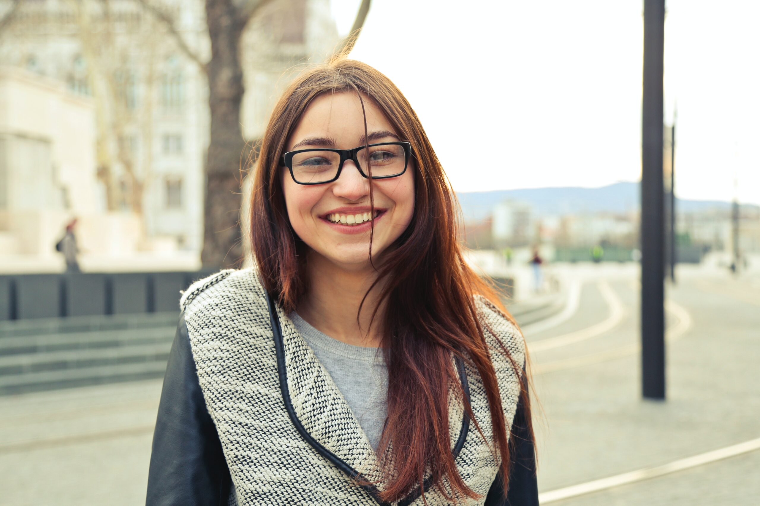 Latina teen smiling with glasses standing outside by the light rail in Denver