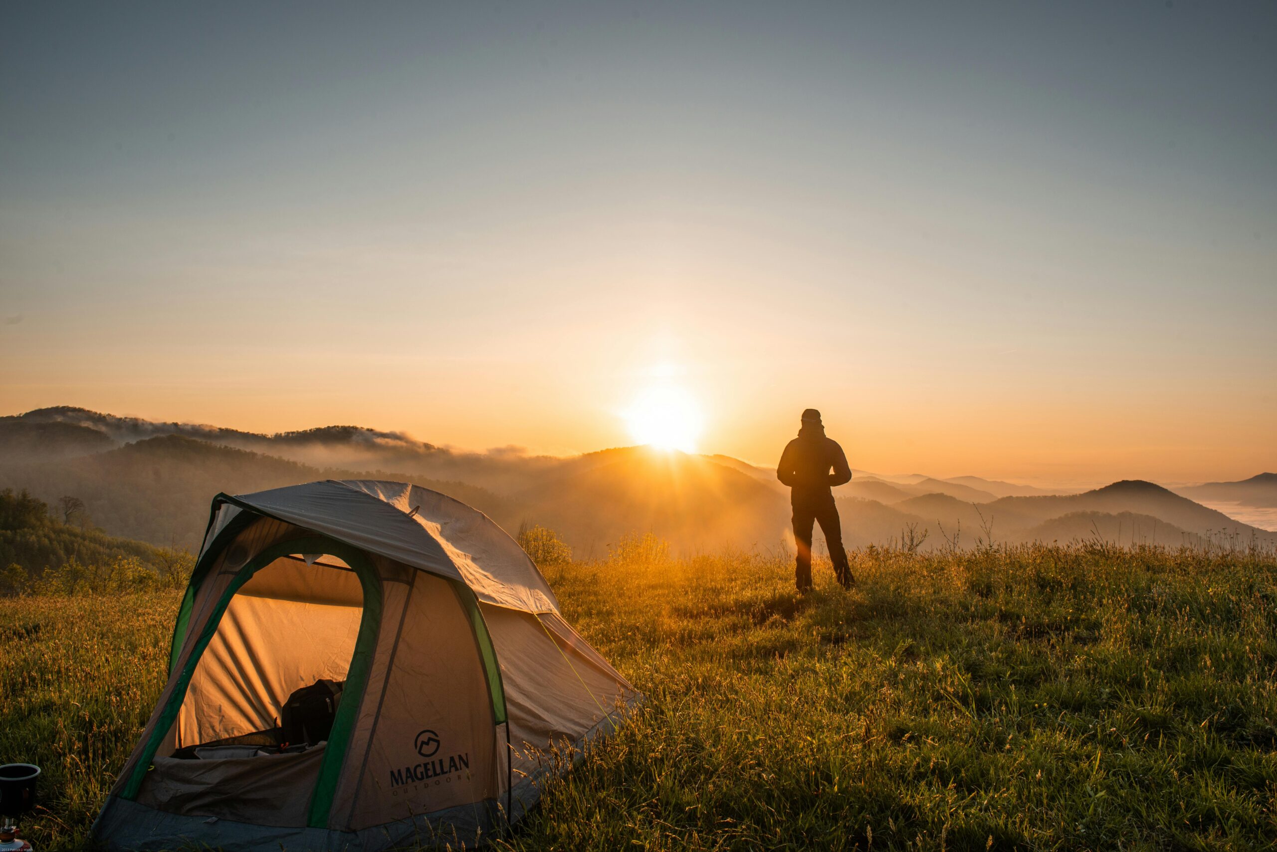 Person camping to support mental health, image of tent and person standing and watching the sun set over the mountains in Colorado