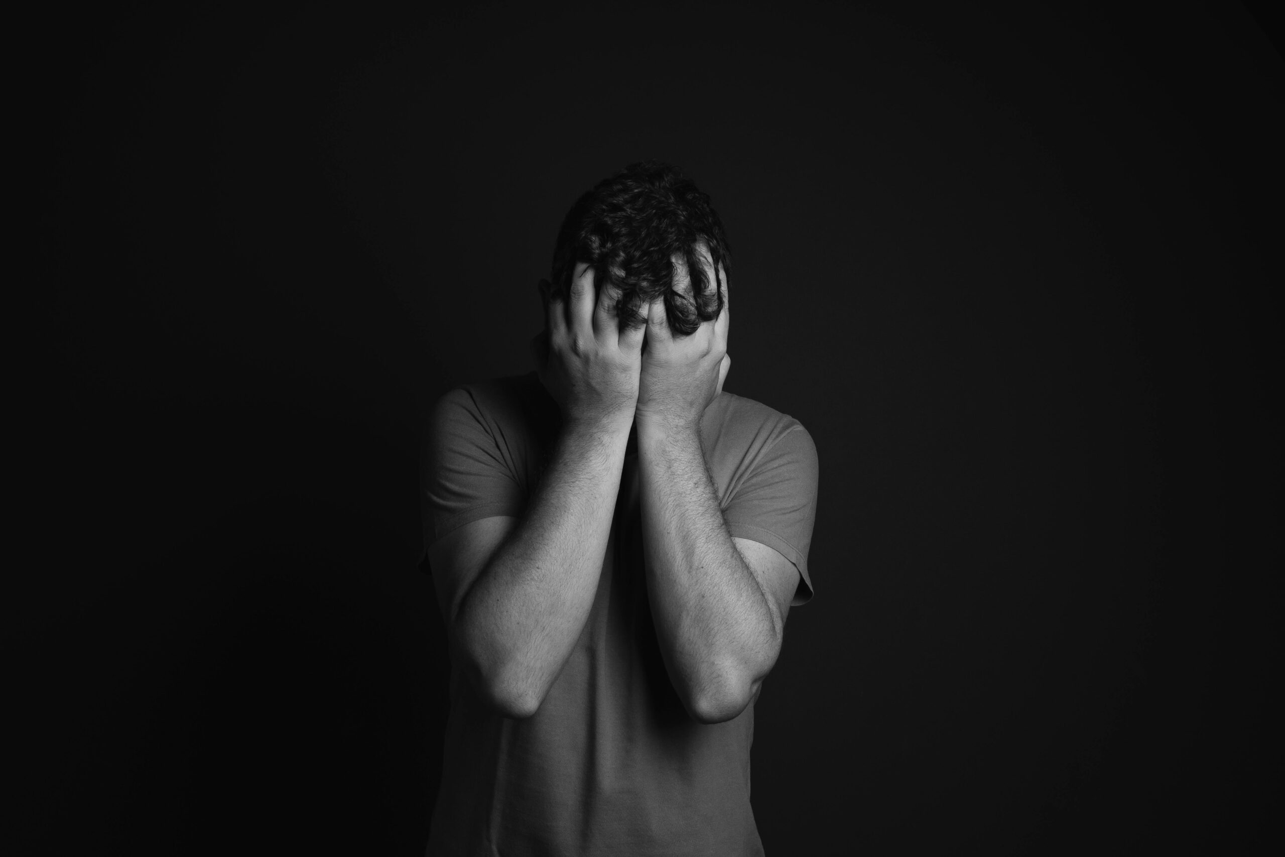depressed teen male, black and white image of teen covering face with hands
