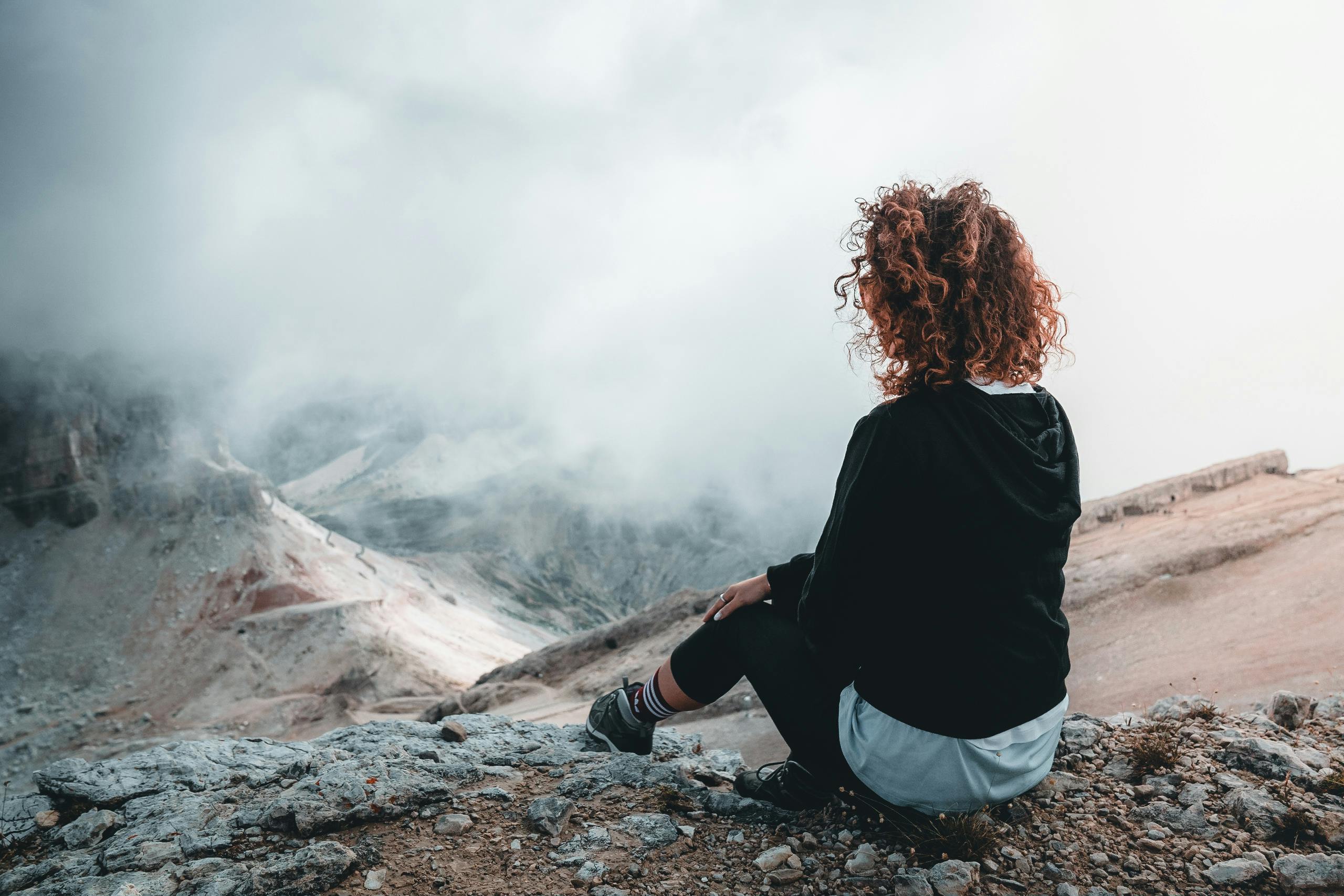 Woman sitting on top of a mountain looking out over the fog facing impact of complex trauma and healing through therapy for complex trauma