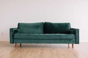 Image of a forest green couch in a room with white walls and wood floors.